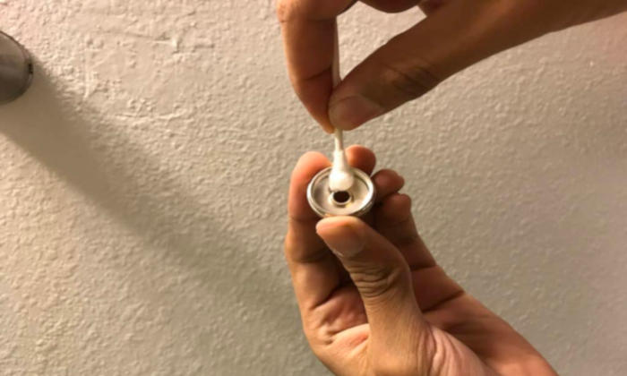 Hands cleaning a trumpet valve cap with a cotton swab