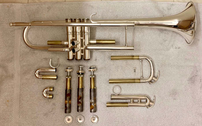 Disassembled trumpet with parts laying on off-white towel