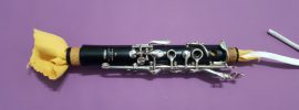 Clarinet upper joint with swab running through it on violet background