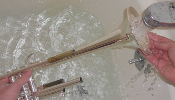 Rinsing a trumpet horn with water in a bathtub