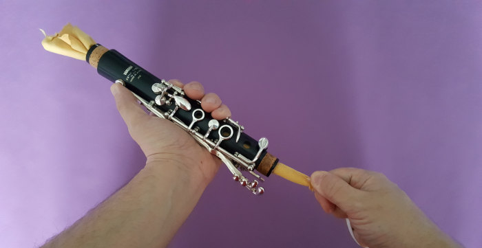 I man cleaning a clarinet upper joint by pulling a swab through on a purple background