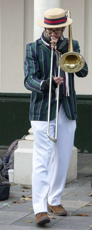 A man playing trombone on a city street and wearing a barbershop quartet outfit