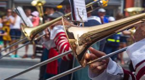 A line of brass musicians performing in an urban street with two trombonists in the foreground