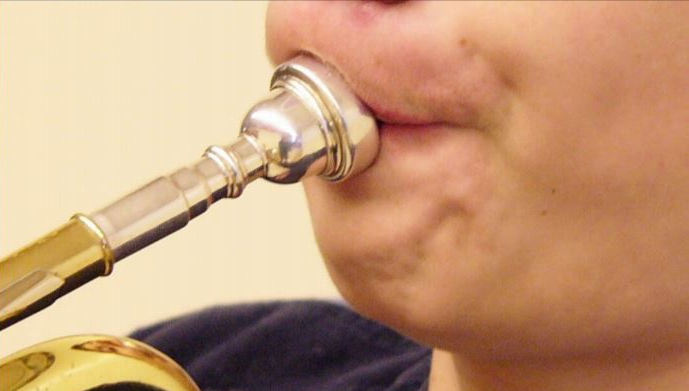 Boy playing trumpet with imperfect embouchure showing chin bunched