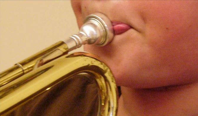 Boy playing trumpet with imperfect embouchure showing sides of mouth pointing downward