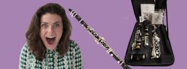 Woman looking excited next to Buffet Prodige clarinet with case and accessories on purple background