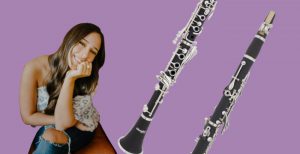 Brown-haired woman sitting in a brown leather chair beside two clarinets on purple background
