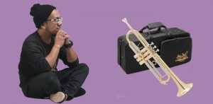 Asian man in dark clothing sitting cross legged looking at a Jean Paul USA TR-330 standard trumpet on a purple background