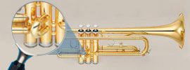 Trumpet with a magnifying glass focused on the second valve slide on grey background