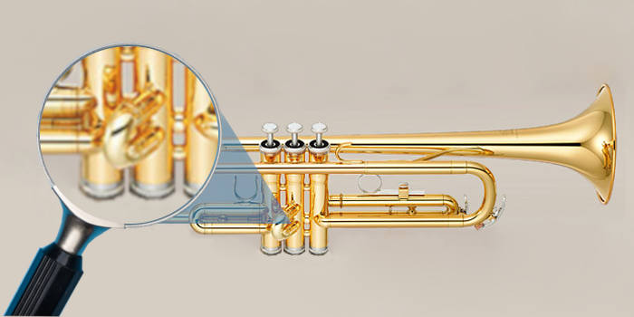 Trumpet with a magnifying glass focused on the second valve slide on grey background