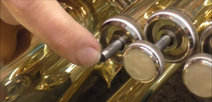 A finger pointing to the valve stem on a trumpet